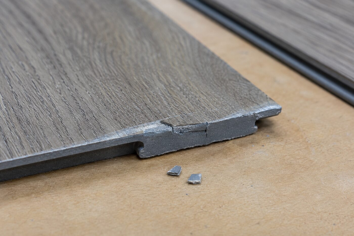 Macro view of a rigid vinyl plank with a cracked click-lock edge and two small broken fragments.